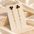 Black clover and gold-tone chain tassel earrings, styled background